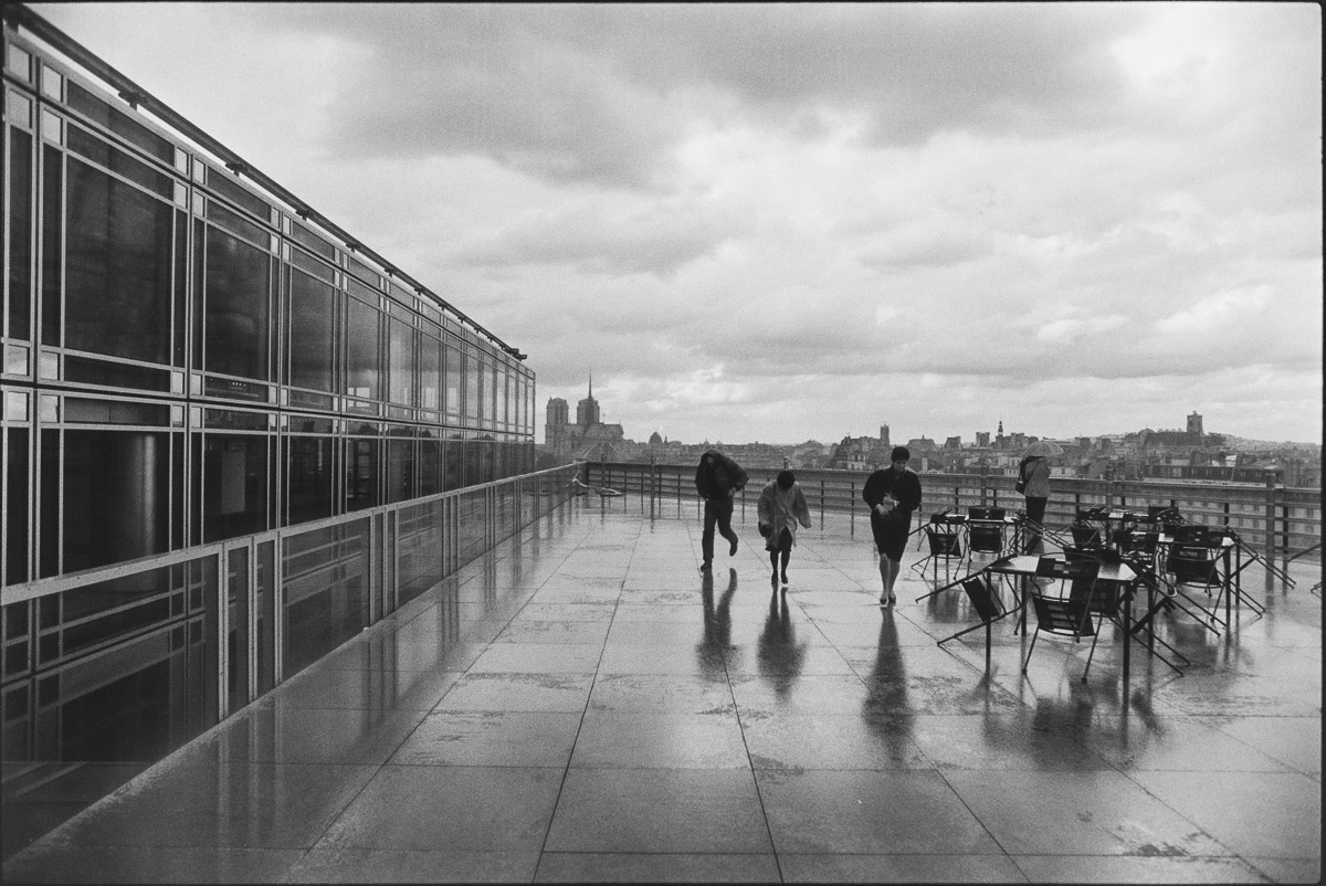 Terrasse mouillée de l’Institut du Monde Arabe en 1989, silhouettes qui courent sous l’averse, photographie argentique en noir et blanc